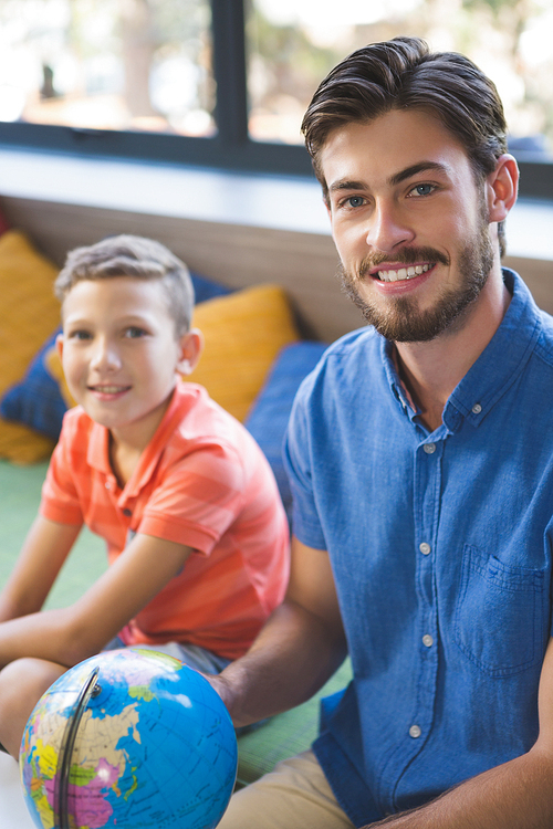 Portrait of teacher and kid discussing globe in library at school