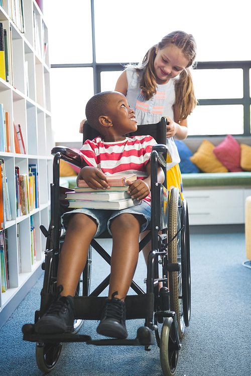 Happy schoolgirl carrying schoolboy in wheelchair at library