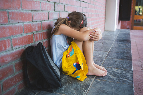 Sad schoolkid sitting alone in corridor at school