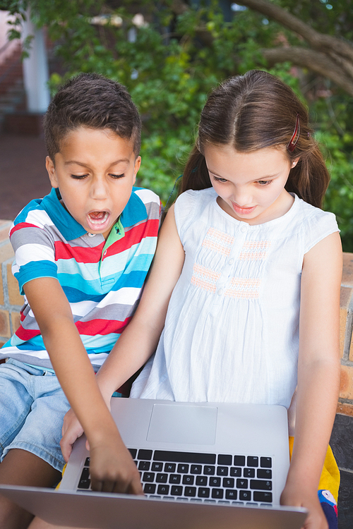 Excited schoolkids using laptop in school campus