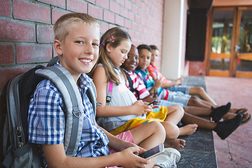 Schoolkids sitting in corridor and using mobile phone at school