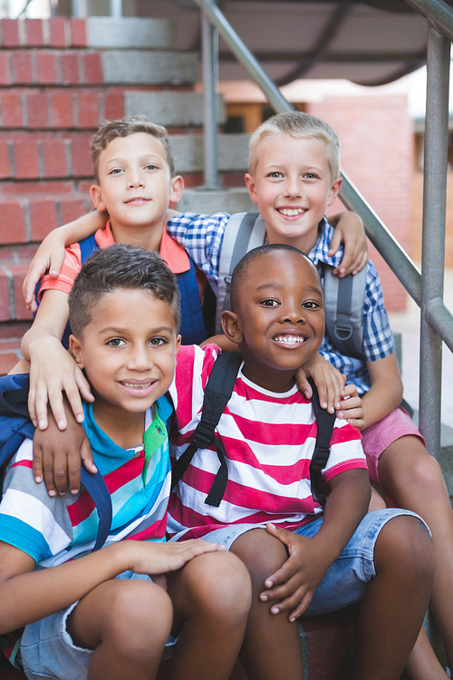 Portrait of smiling schoolkids sitting with arms around on staircase at school