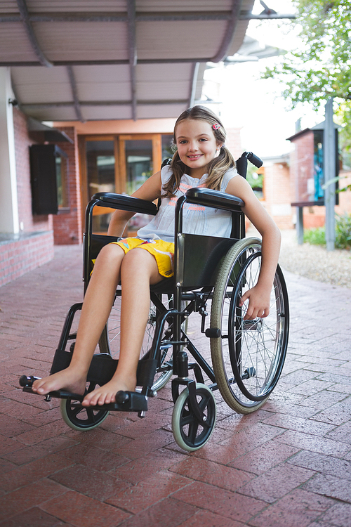 Portrait of cute girl sitting on wheelchair in corridor at school