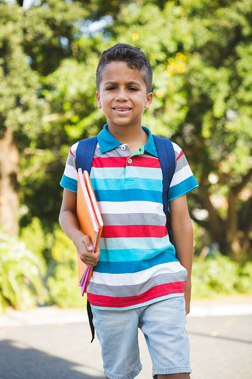 Portrait of happy schoolboy holding book and walking in campus