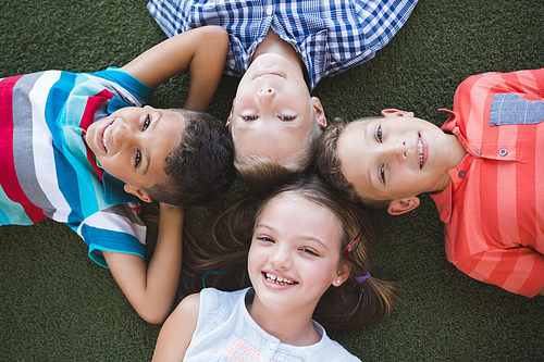 Portrait of smiling schoolkids lying on grass in campus at school