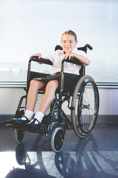 Portrait of happy schoolkid sitting on wheelchair in classroom at school