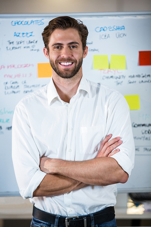 Portrait of confident businessman with arms crossed standing against whiteboard in office