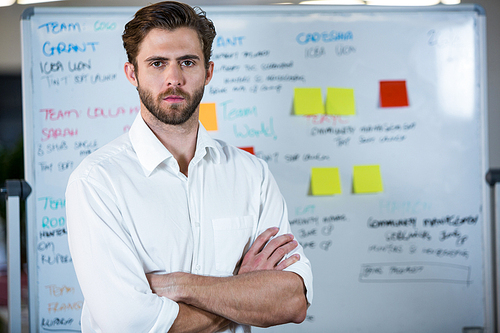 Portrait of confident businessman standing against whiteboard in office