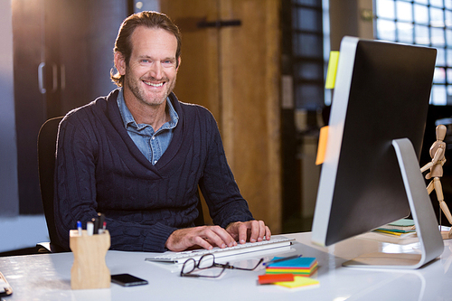 Portrait of happy businessman working on computer in creative office
