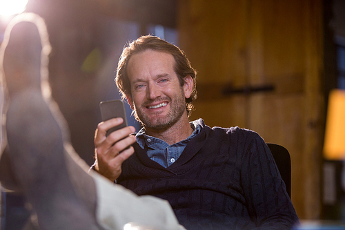 Portrait of smiling businessman holding cellphone while relaxing in creative office