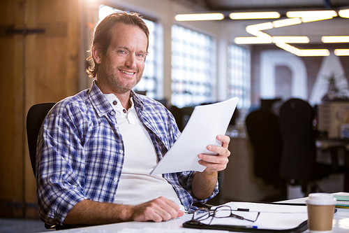Portrait of businessman holding documents while sitting at desk in creative office