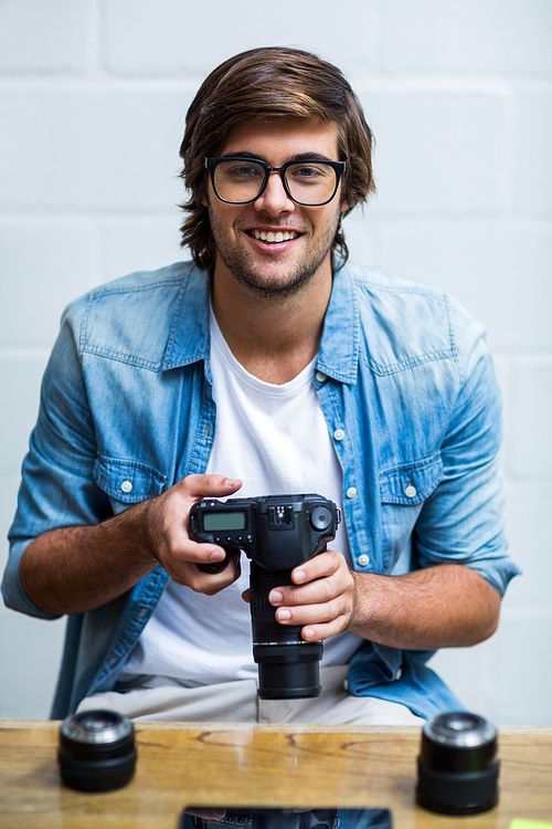 Portrait of happy young man holding camera in creative office