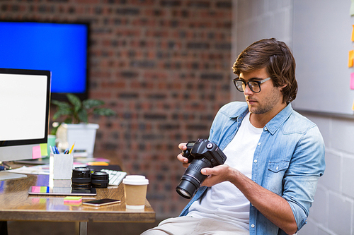 Young man holding camera by table in creative office