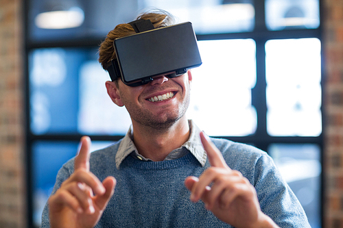 Smiling businessman gesturing while using virtual reality headset in creative office