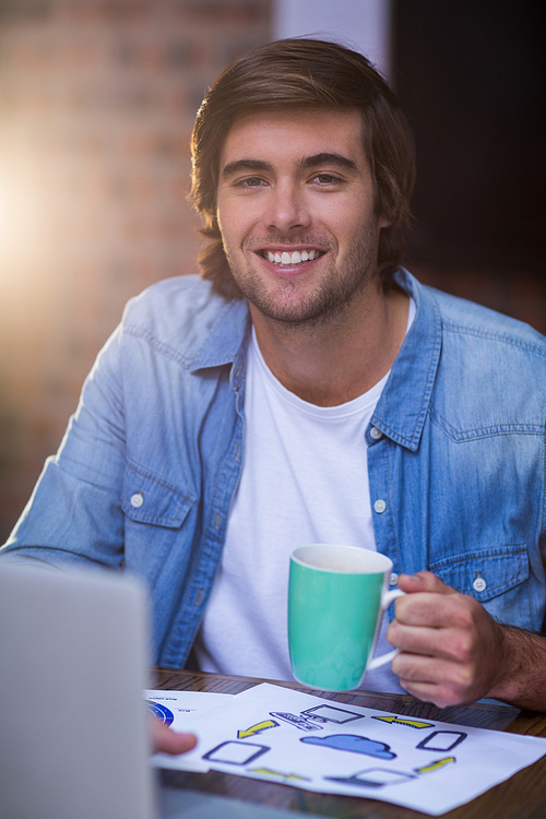Portrait of young businessman having coffee in creative office