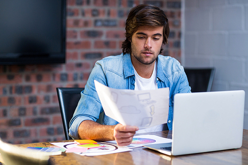 Creative businessman reading document at desk in office