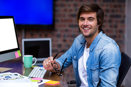 Portrait of young businessman sitting at desk in creative office