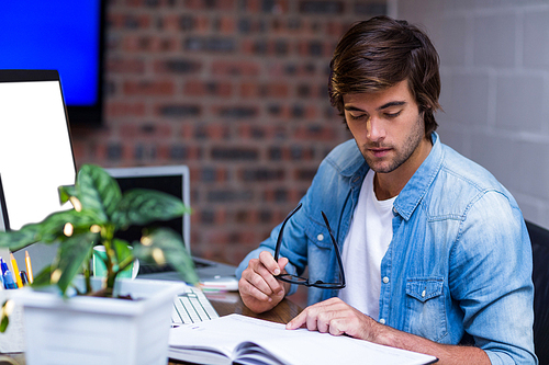 Young businessman reading book at desk in creative office
