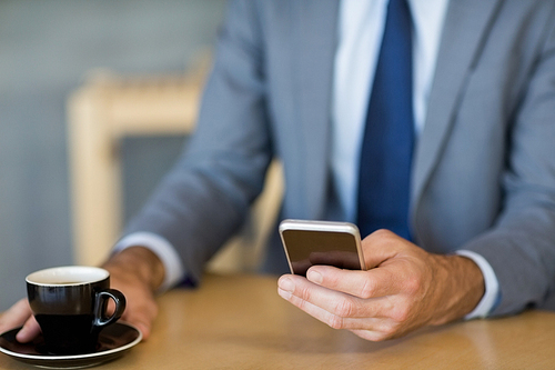 Mid-section of businessman using mobile phone while having a cup of tea in restaurant