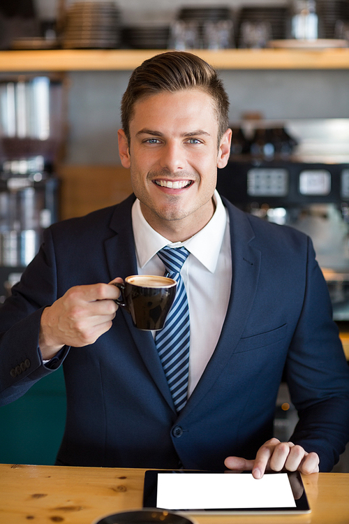 Portrait of businessman using digital tablet while having coffee in cafÃ©
