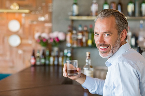 Portrait of man sitting at bar counter holding glass of whiskey in restaurant