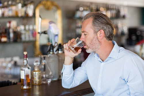 Serious man drinking whiskey at bar counter in restaurant
