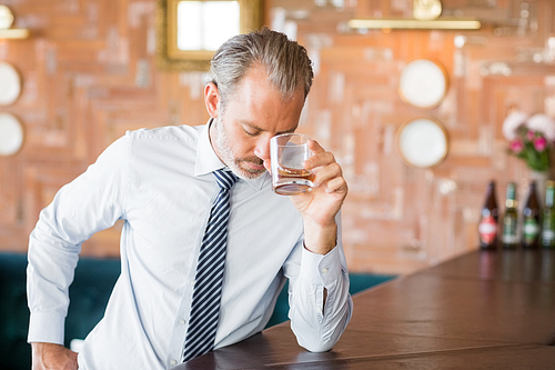 Businessman clutching whiskey glass to forehead on bar counter