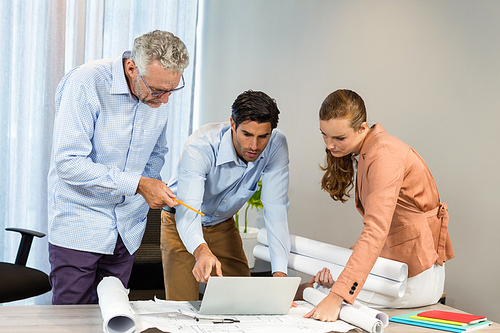 Businesswoman and coworkers discussing blueprint using laptop in the office