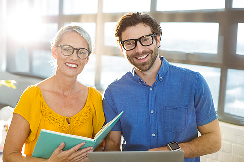 Portrait of smiling business executives holding document and laptop in office