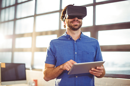 Male business executive in virtual reality headset using digital tablet in office