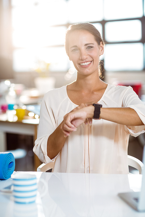 Portrait of business executive sitting on chair and adjusting a smartwatch in office