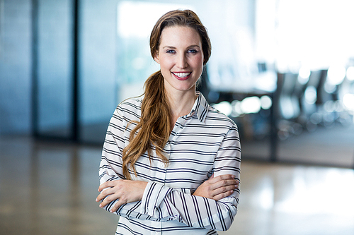 Portrait of smiling woman standing with arms crossed in office
