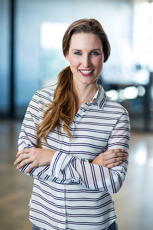 Portrait of smiling woman standing with arms crossed in office