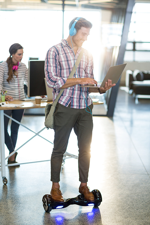 Smiling man standing on hoverboard and using laptop in office