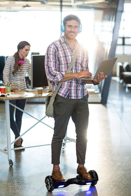 Portrait of smiling man standing on hoverboard and using laptop in office