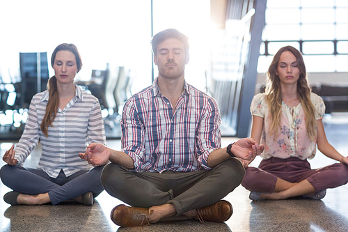 Business people performing yoga on floor in office