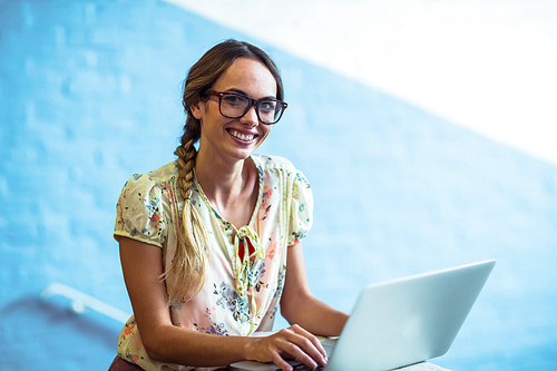 Portrait of woman standing near staircase and using laptop in office