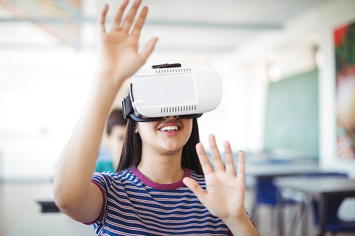 Schoolgirl using virtual reality headset in classroom at school