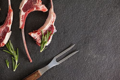 Rib chops, rosemary herb and fork against black background