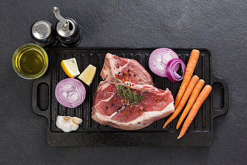 Sirloin chop and ingredients on black grill against black background