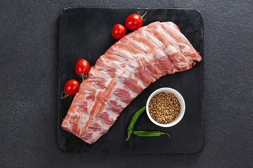Beef ribs, cherry tomatoes and coriander seeds against black background