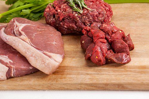 Sirloin chop, beef patty and diced beef on wooden board against white background
