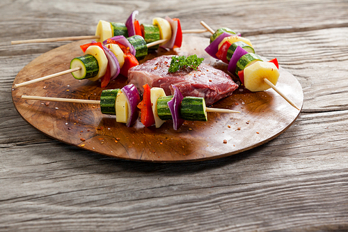 Sirloin chop and skewered vegetables on wooden board against wooden background