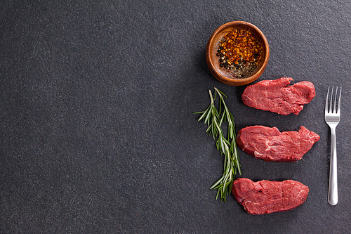 Beef steak, rosemary herb and spices against black background