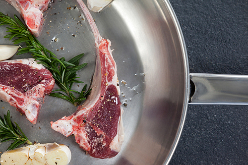 Rib chop and herbs in frying pan against black background