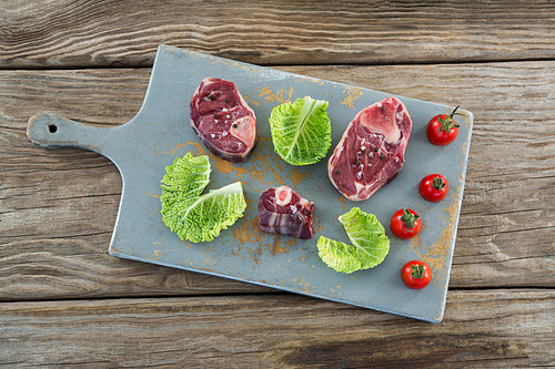 Sirloin steak, cherry tomatoes and cabbage leaves on board against wooden background
