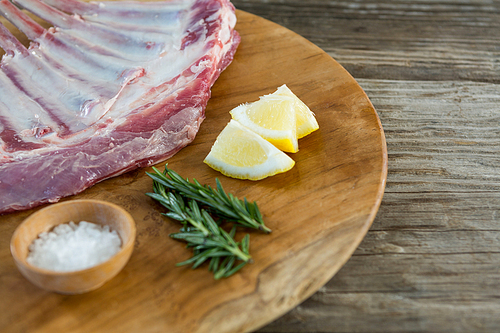 Raw Beef ribs rack, rosemary herb, salt and lemon on wooden tray against wooden background