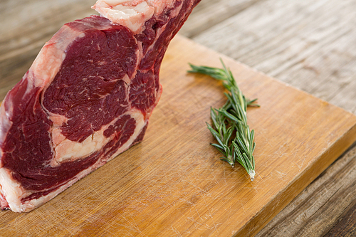 Raw Rib chop steak and rosemary herb on wooden board against wooden background