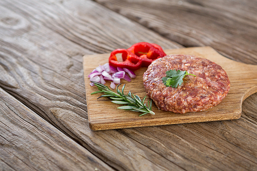 Raw beef patty and ingredients on wooden tray against wooden background