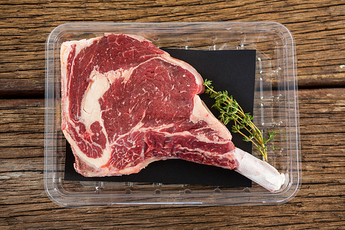 Rib chop and herbs in plastic box against wooden background